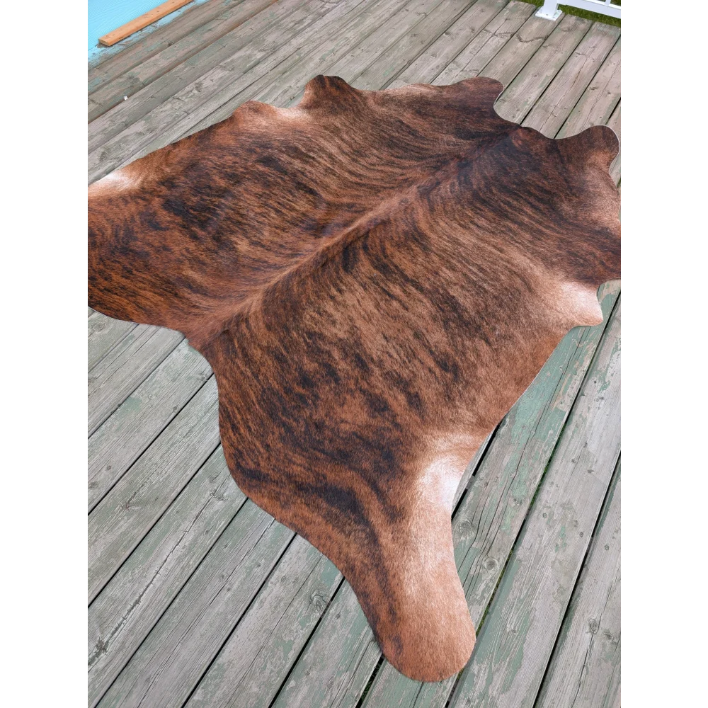 Large brown and black cowhide rug with natural fur texture showcasing unique characteristics on wooden deck