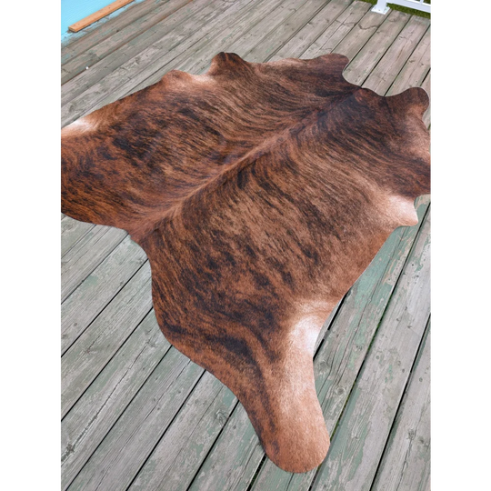 Large brown and black cowhide rug with natural fur texture showcasing unique characteristics on wooden deck