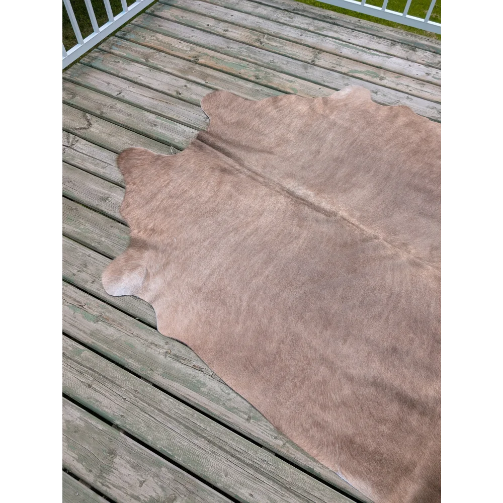 A large cowhide rug with unique characteristics in soft light brown natural fur lies flat on weathered wooden deck planks