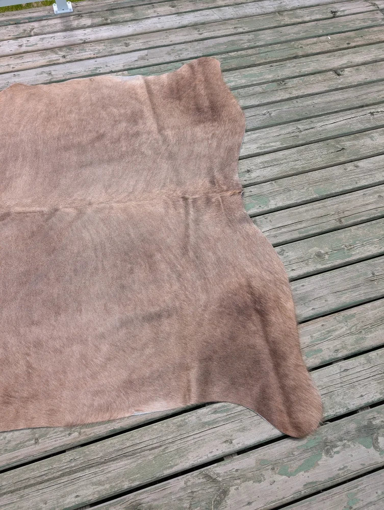 Large cowhide rug in light brown with unique characteristics and a soft, slightly textured surface measuring 73.5 x 68 inches