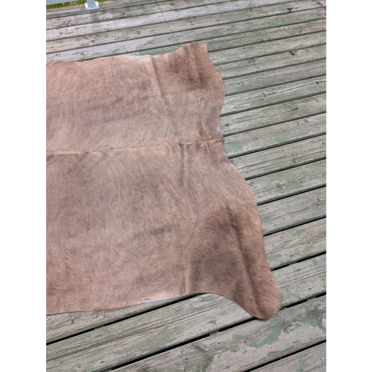 Large cowhide rug in light brown with unique characteristics and a soft, slightly textured surface measuring 73.5 x 68 inches