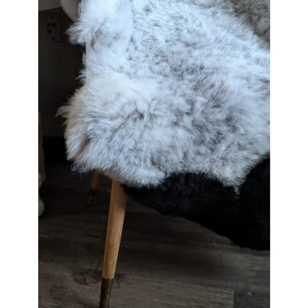 A plush white and gray medium spotted icelandic sheepskin rug draped over a wooden leg chair
