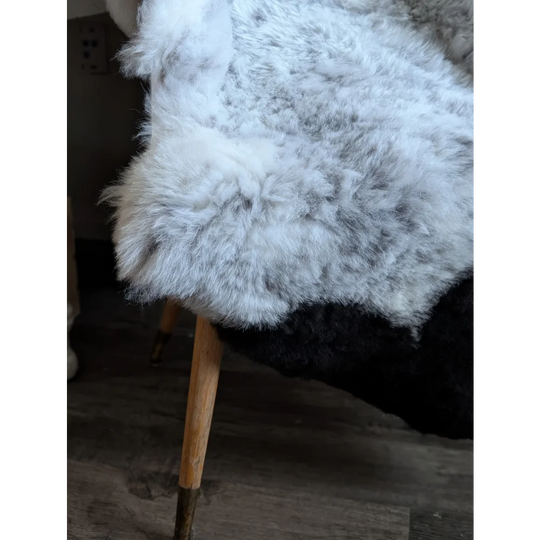 A plush white and gray medium spotted icelandic sheepskin rug draped over a wooden leg chair