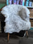 A large spotted icelandic sheepskin rug with soft white and gray gradient draped over a wooden chair back