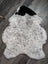 A large 46 x 34 inch plush spotted icelandic sheepskin rug with soft white gray fur and a black patch on top left side