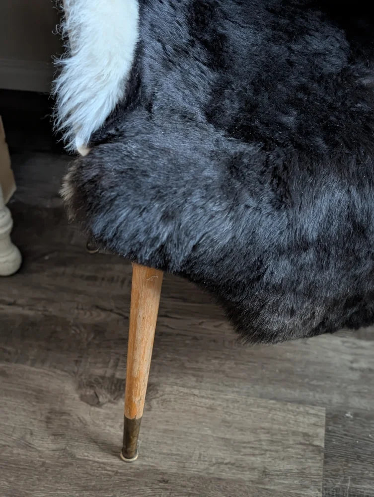 Black and white icelandic sheepskin throw with short wool draped over a wooden chair leg with brass metal cap