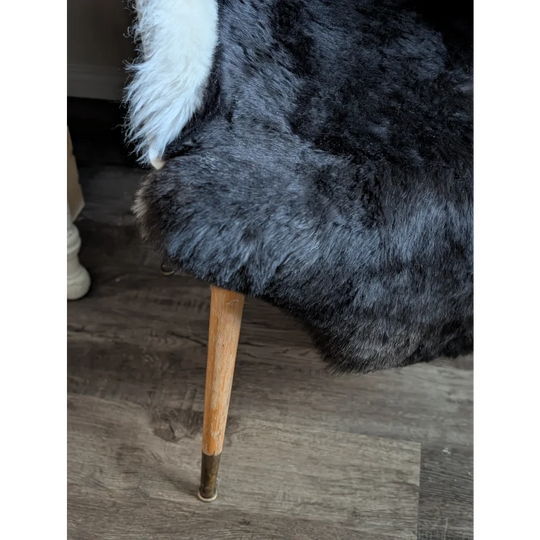 Black and white icelandic sheepskin throw with short wool draped over a wooden chair leg with brass metal cap