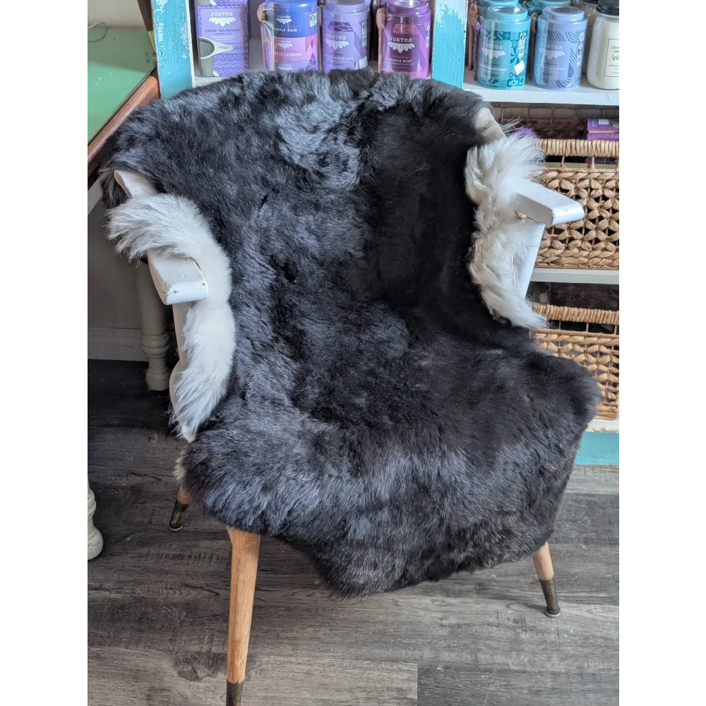 A dark gray icelandic sheepskin rug with white short wool trim draped over a vintage wooden chair