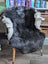 A dark gray icelandic sheepskin rug with white short wool trim draped over a vintage wooden chair