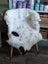 A plush white and black medium spotted icelandic sheepskin rug draped over a wooden chair with metal legs