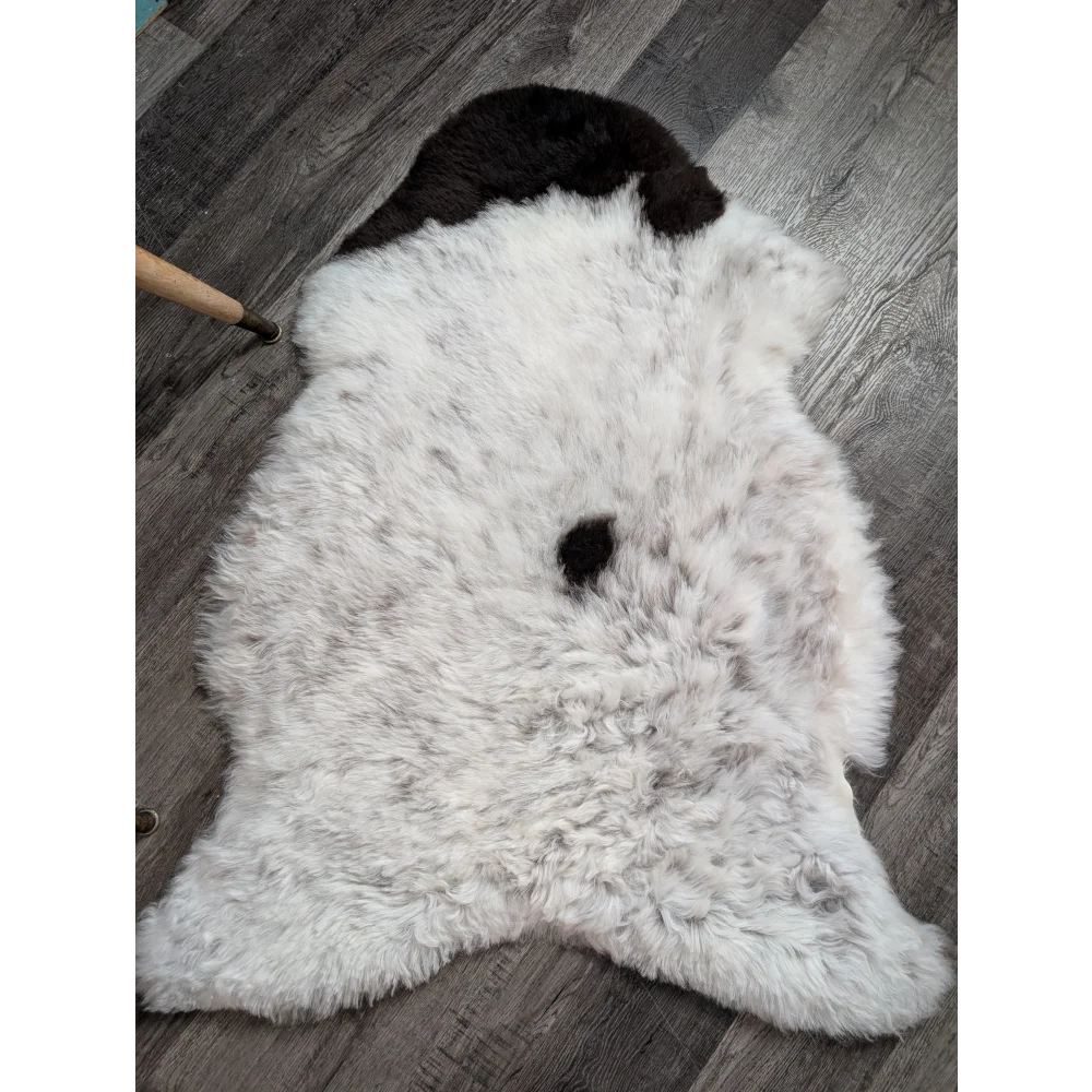 A plush white medium spotted icelandic sheepskin rug with soft wool and two distinct black patches near the top