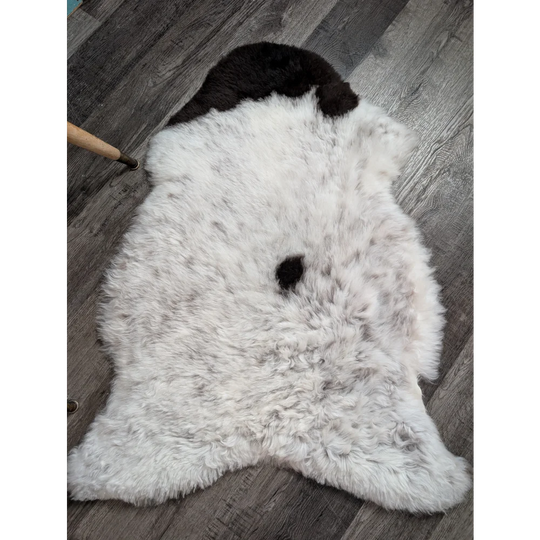 A plush white medium spotted icelandic sheepskin rug with soft wool and two distinct black patches near the top