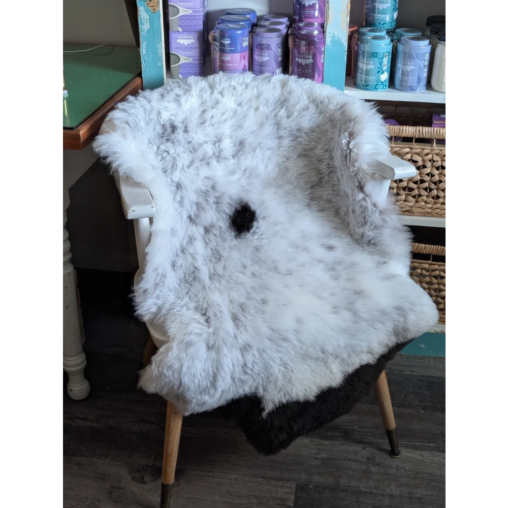 A fluffy white and gray medium spotted icelandic sheepskin rug draped over a wooden chair with a black spot