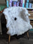 A fluffy white and gray medium spotted icelandic sheepskin rug draped over a wooden chair with a black spot