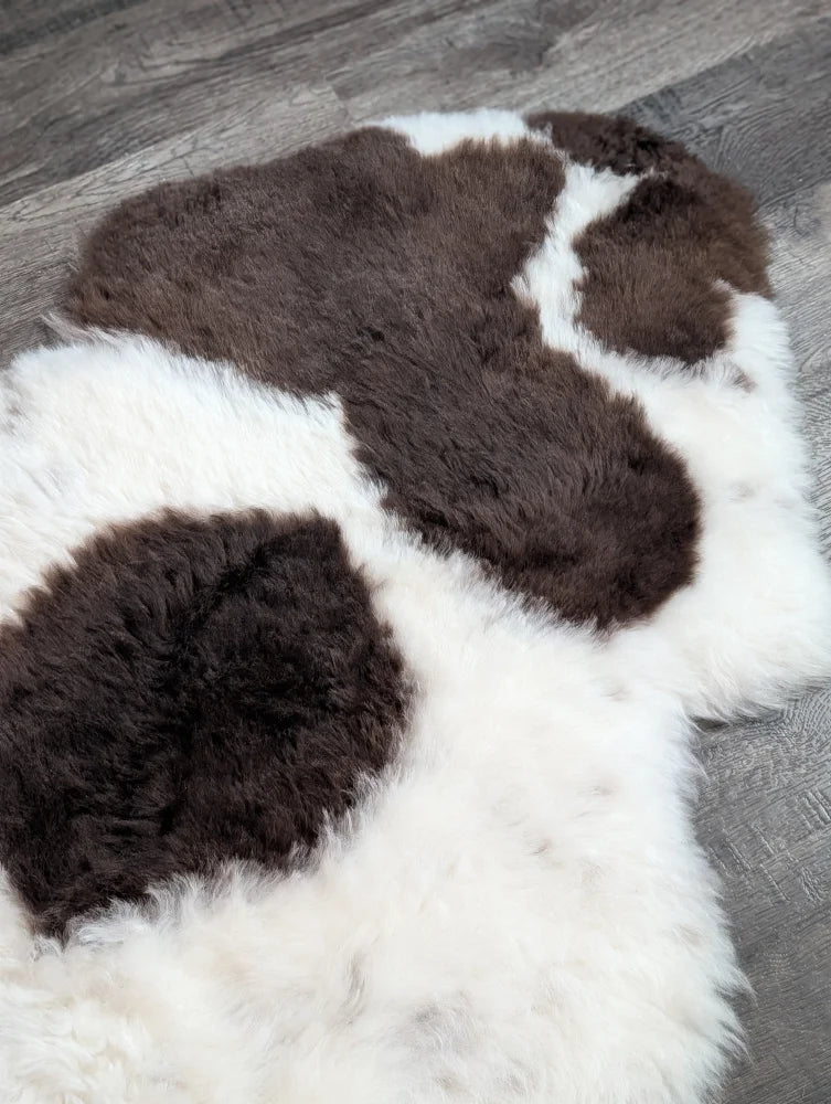 A large plush spotted icelandic sheepskin rug with natural brown and white cow print short wool fibers
