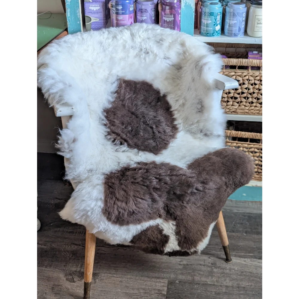 A cozy white and brown spotted icelandic sheepskin rug draped over a wooden armchair with a cowhide fur look