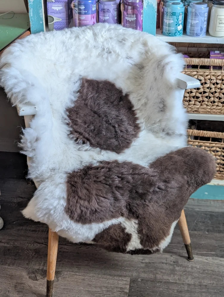 A cozy white and brown spotted icelandic sheepskin rug draped over a wooden armchair with a cowhide fur look