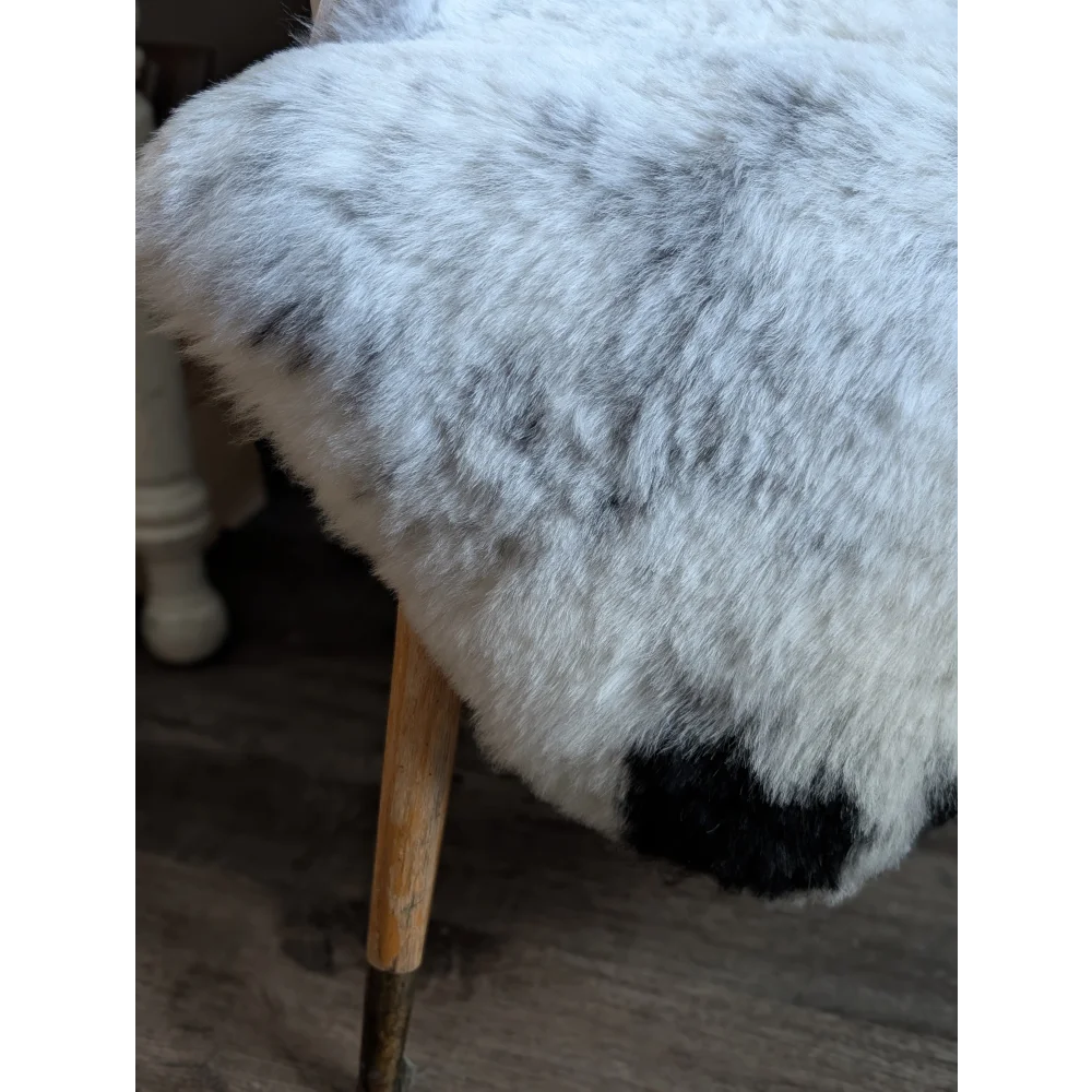 A plush gray and white spotted icelandic sheepskin rug draped over a wooden stool with soft fluffy texture