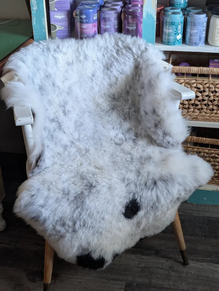 A plush white and gray spotted icelandic sheepskin rug with black paw prints draped over a wooden chair