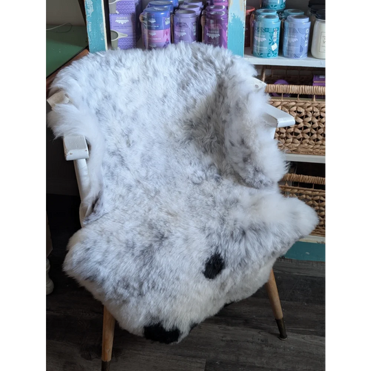 A plush white and gray spotted icelandic sheepskin rug with black paw prints draped over a wooden chair