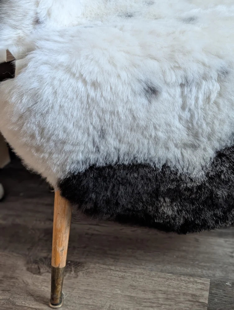 White and black sheepskin-covered stool with wooden legs featuring a spotted icelandic sheepskin rug look