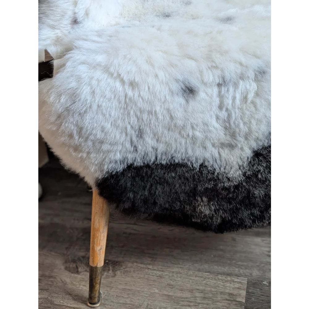 White and black sheepskin-covered stool with wooden legs featuring a spotted icelandic sheepskin rug look