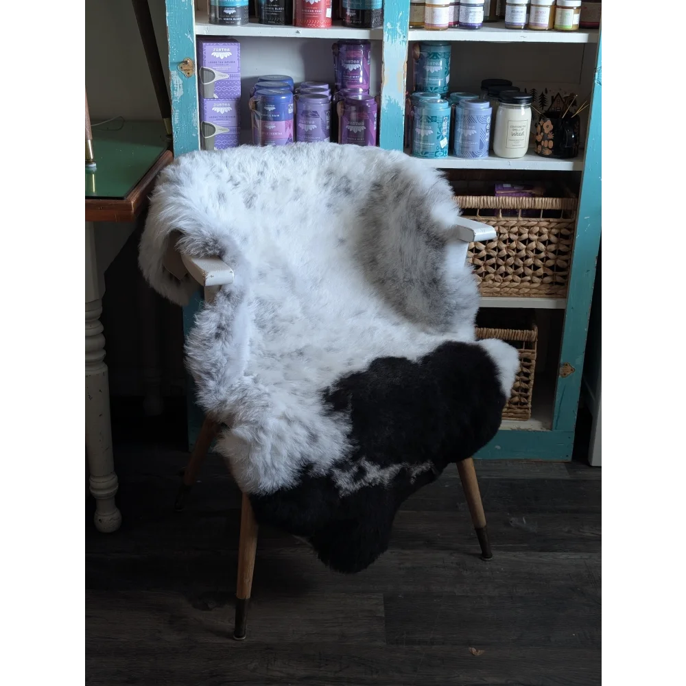 A plush black and white spotted icelandic sheepskin rug draped over a wooden chair with light legs