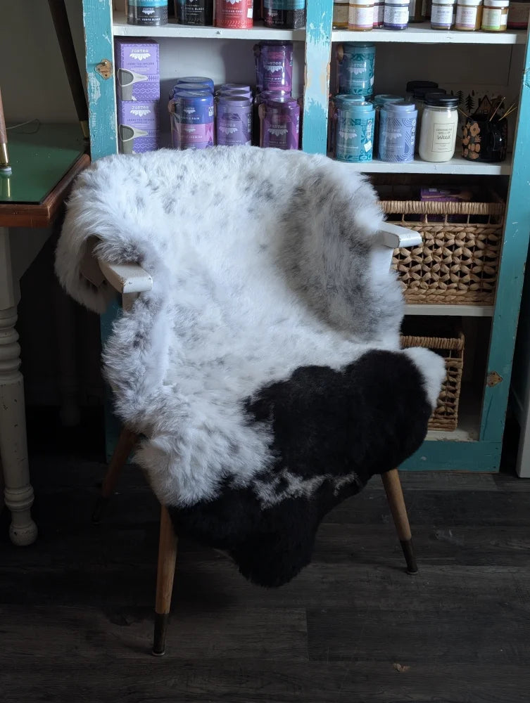 A plush black and white spotted icelandic sheepskin rug draped over a wooden chair with light legs