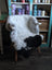 A plush black and white spotted icelandic sheepskin rug draped over a wooden chair with light legs