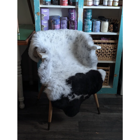 A plush black and white spotted icelandic sheepskin rug draped over a wooden chair with light legs