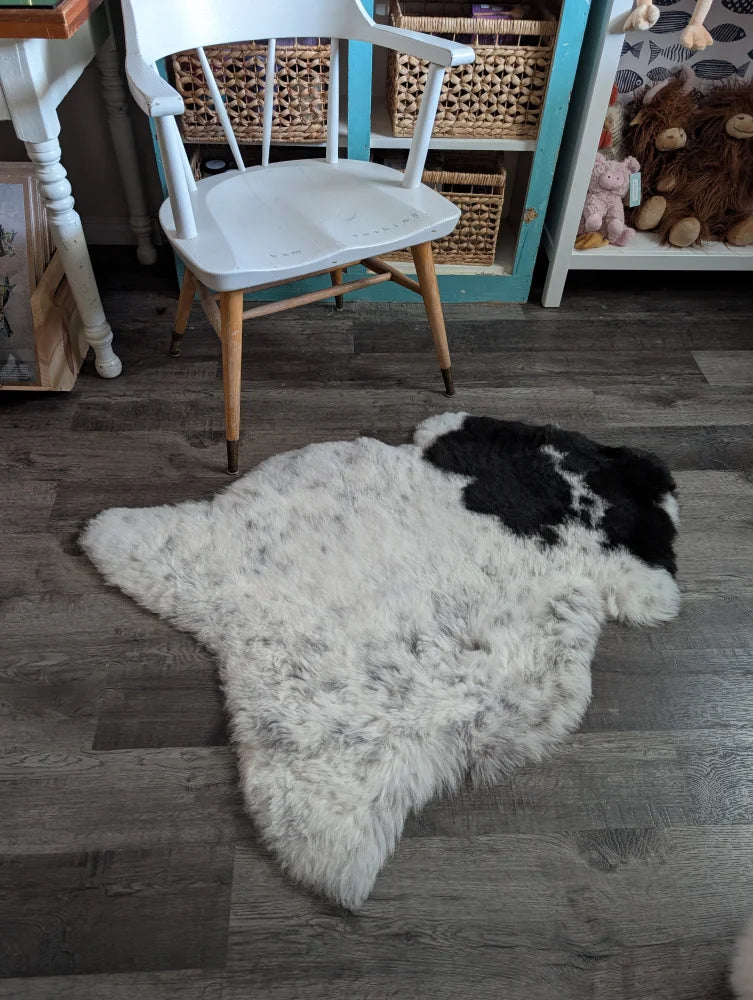 A fluffy white and black medium spotted icelandic sheepskin rug with natural fur texture lying on the floor