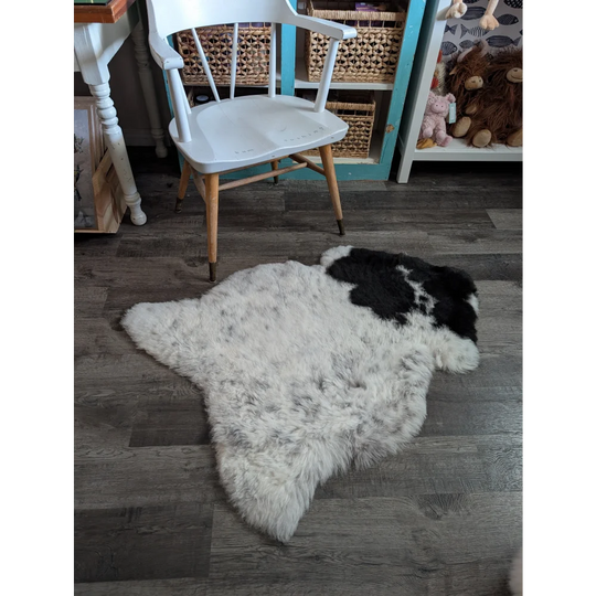 A fluffy white and black medium spotted icelandic sheepskin rug with natural fur texture lying on the floor