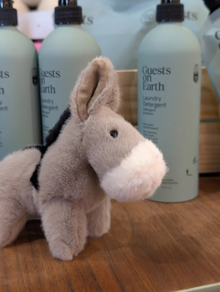 A soft plush gray donkey toy called the donkey with a white muzzle and black fabric harness