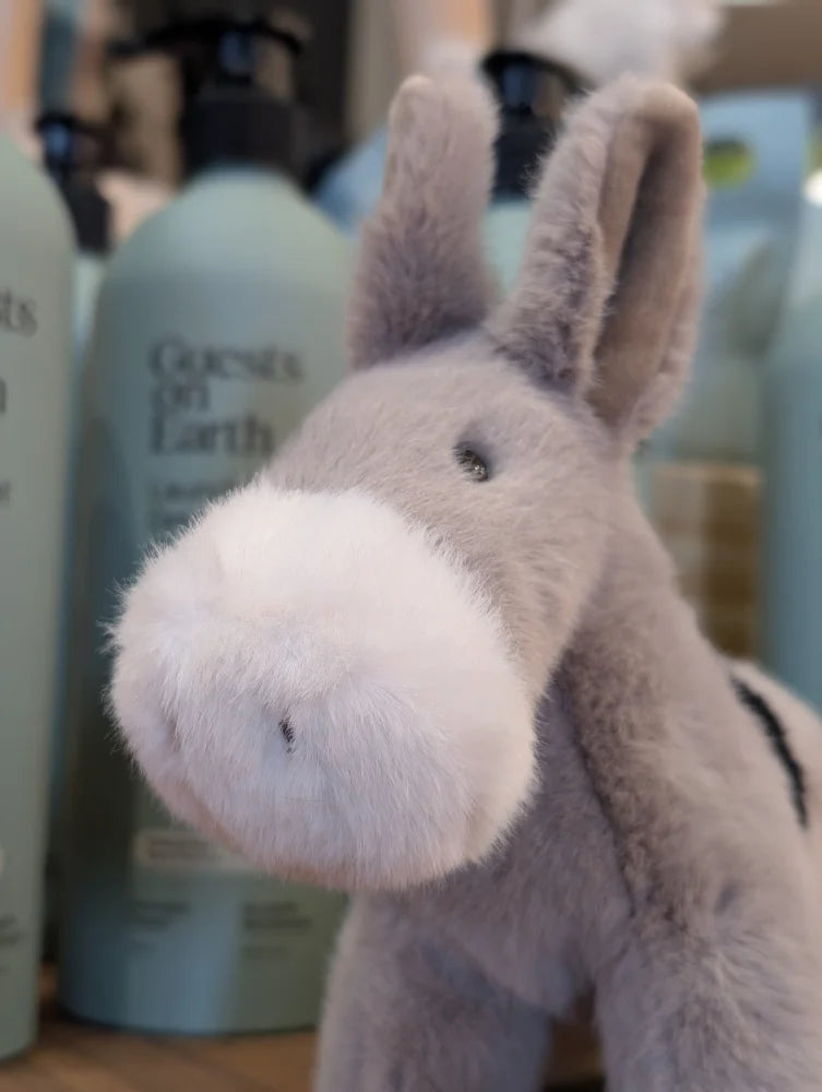 A soft gray plush donkey toy called the donkey with a fluffy white muzzle and black embroidered eyes