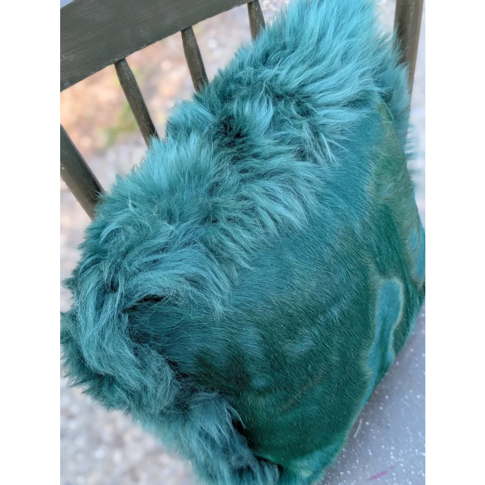 The green cushion is a plush teal faux fur throw blanket with soft shaggy texture, dyed green for a cozy vibe