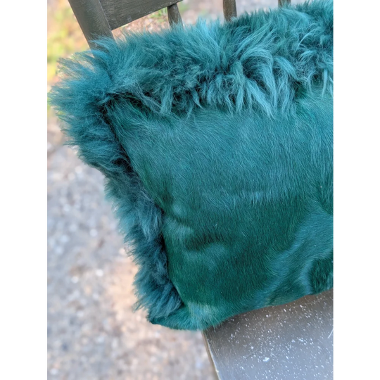 The green cushion is a teal faux fur throw pillow with plush shaggy texture and soft dense pile dyed green style