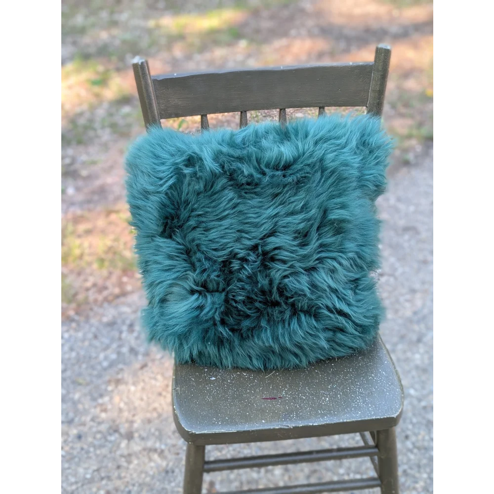 The green cushion is a teal dyed green faux fur throw pillow with a plush shaggy texture perfect for cozy decor
