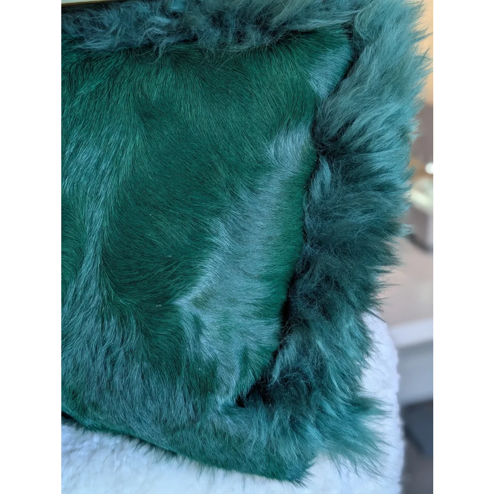 The green cushion is an emerald dyed green faux fur throw pillow with a plush texture and soft fluffy fringe edges