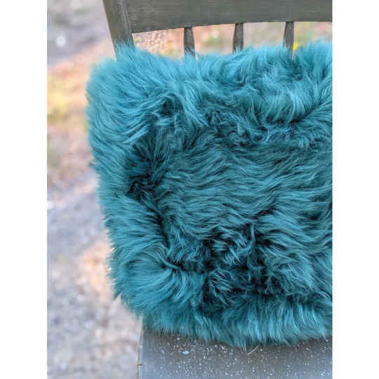The green cushion is a plush teal faux fur throw blanket with a soft shaggy texture dyed green for cozy vibes