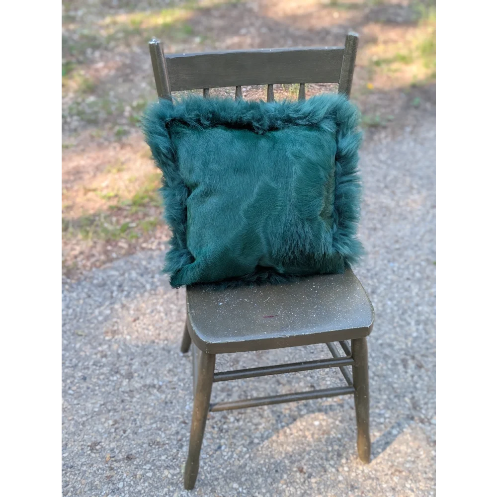 The green cushion is a plush teal fur pillow with a soft fluffy texture and dyed green accents on an old wooden chair