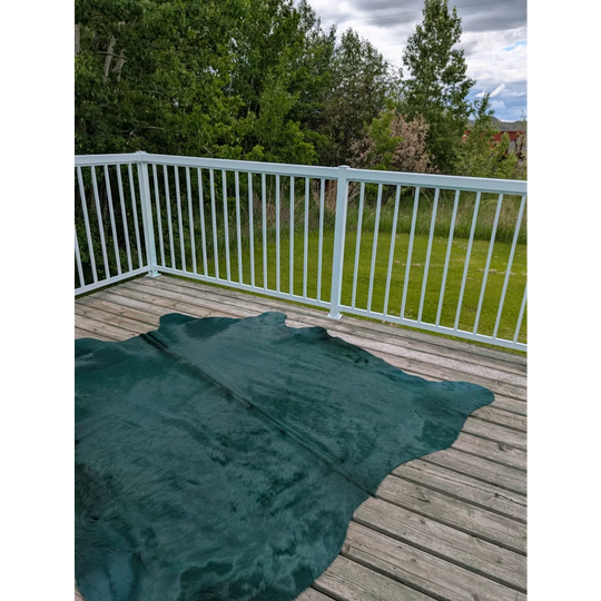 Dark green dyed green angus oliver green cowhide rug laid out on a wooden deck called the green cushion