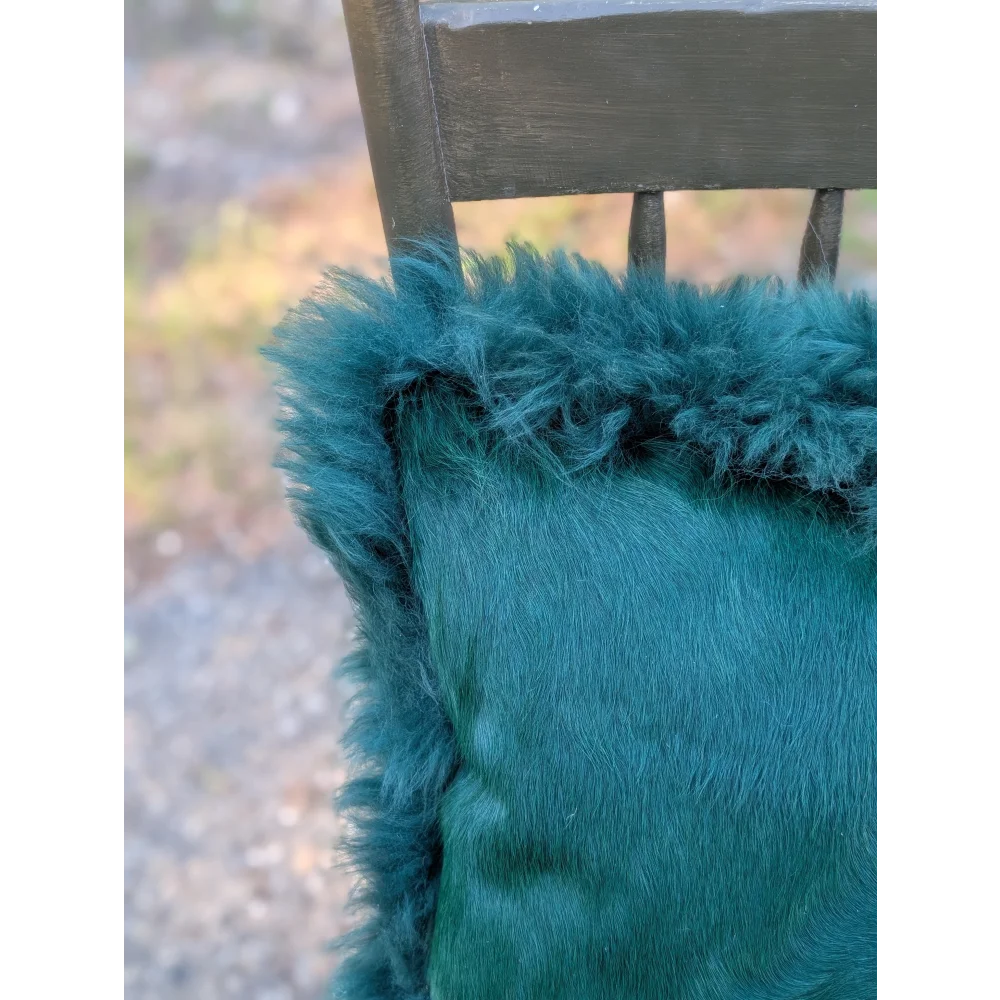The green cushion is a teal dyed green plush fur throw pillow with a soft texture and slightly frayed edges by angus oliver