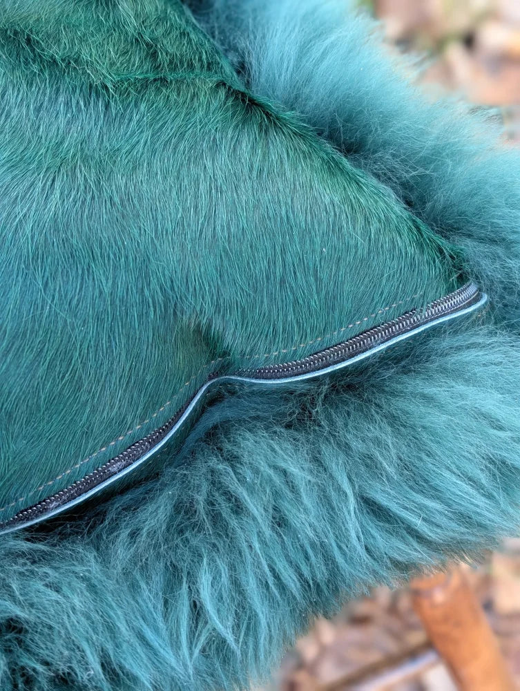 Teal faux fur coat with black zipper detail shown from back in woolly green sewing studio with green sheepskin cushion