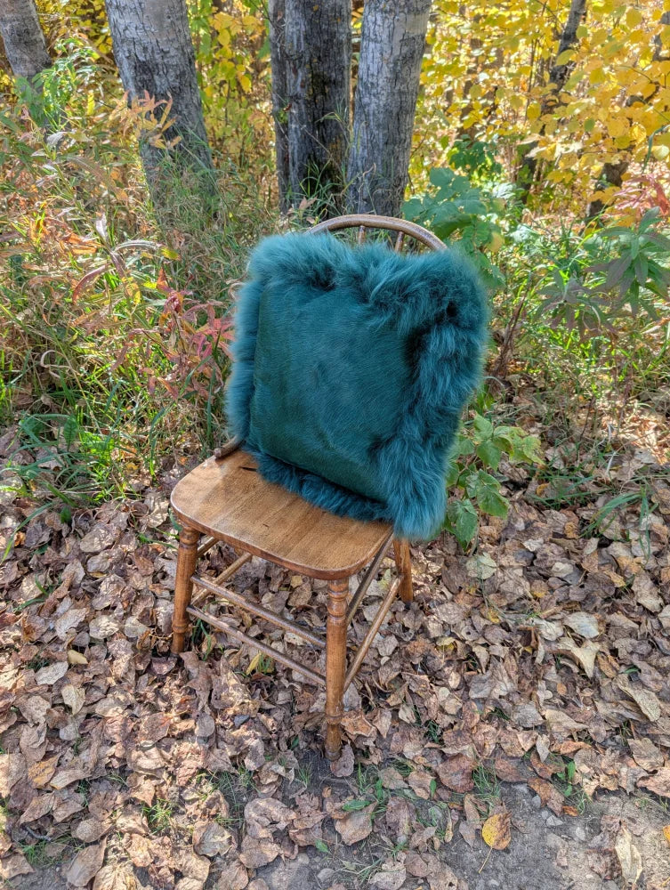 Teal faux fur throw pillow on wooden chair outdoors perfect for a sewing studio with woolly green vibes and green sheepskin look