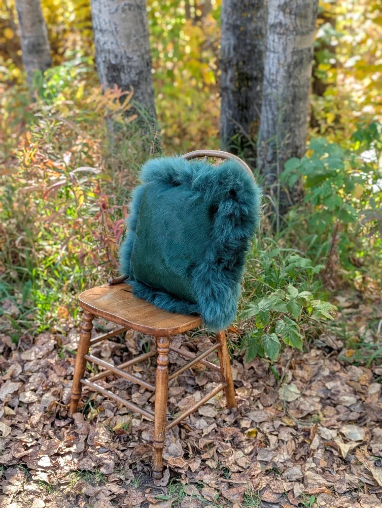 Teal faux fur backpack with plush fluffy texture and rounded top handle featured in green sheepskin sewing studio style