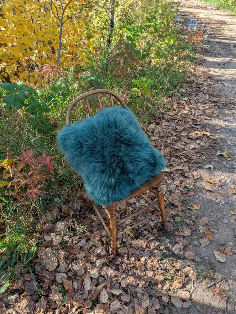 Teal faux fur throw pillow resting on wooden chair complements green sheepskin and woolly green sewing studio vibes
