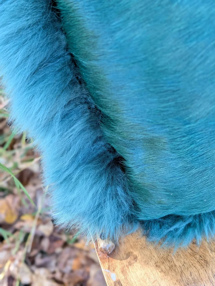A plush green sheepskin cushion with vibrant teal woolly green faux fur and soft uneven edges from the sewing studio