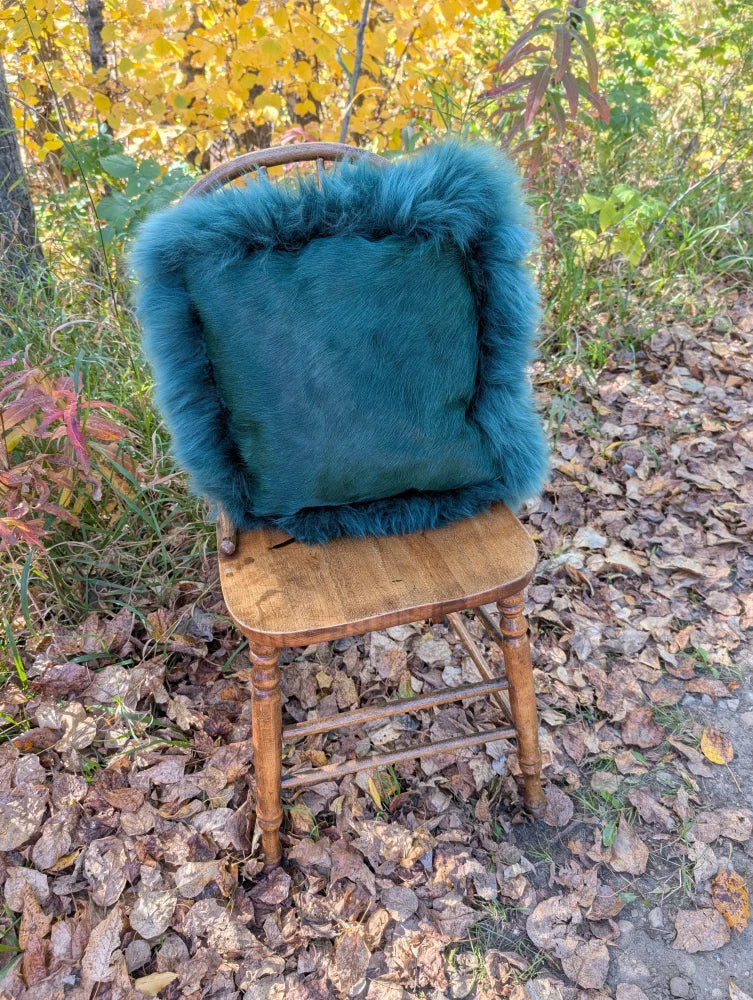 A plush green sheepskin throw pillow with woolly green fur and frayed edges on an old wooden chair in a sewing studio