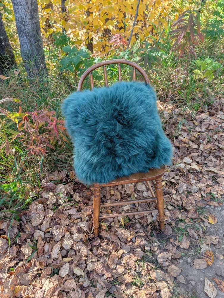 A plush green sheepskin and cowhide cushion with woolly green faux fur on a wooden chair in a sewing studio