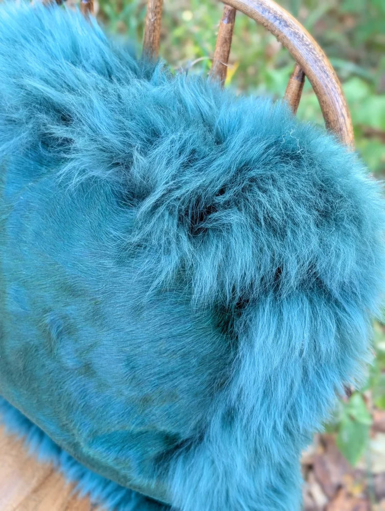 A plush teal blue faux fur throw draped over a chair back perfect for a woolly green sewing studio vibe